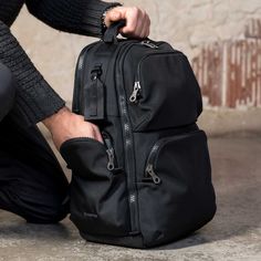 a person holding onto a black backpack on the ground