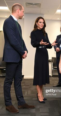 two men and a woman standing in an office talking to each other while one man holds his hand out