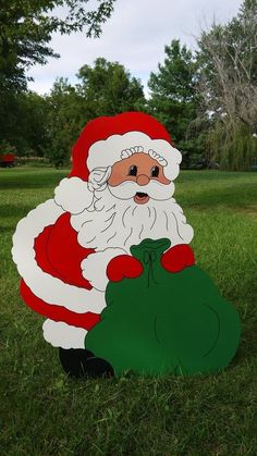 a paper cut out of santa claus holding a bag of gifts in the grass with trees in the background