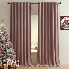 a christmas tree sitting next to a window covered in pink curtain drapes and presents