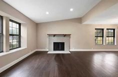 an empty living room with hard wood floors and two windows in the wall, along with a fireplace