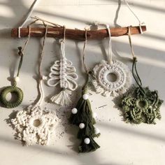 four ornaments hanging from a wooden stick on top of a white wall with some string attached to them