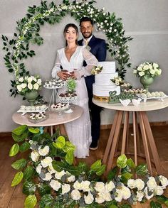 a man and woman standing next to each other in front of a table with cakes on it