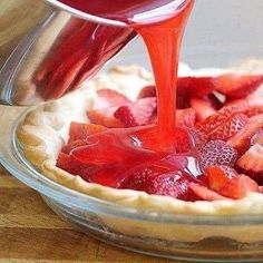 someone pouring syrup onto a pie with strawberries in it