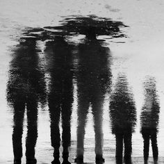 three people are standing in the water with their reflection on the wet ground and one is holding an umbrella