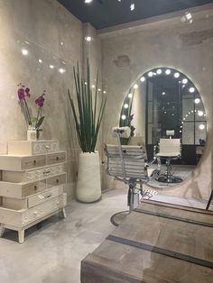 a hair salon with large round mirror and lights on the wall, chairs and desks