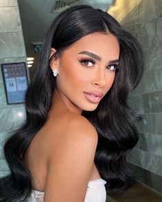 a woman with long black hair wearing a strapless dress and diamond earrings, posing for the camera