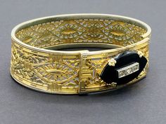 "Beautiful gold filigree bracelet made by Plainville Stock Company in the 1930s. The front panel features a black onyx ellipse set with rhinestones. This is a common theme for mourning jewelry, as it signified \"a light in the darkness\" and was intended to give comfort to the bereaved. I think the sentiment is meaningful even for those who have not lost a loved one, and can be a reminder of goals and important life motifs. CONDITION/SIZE: Good vintage condition - some finish loss which is reall Antique Cuff Bracelet With Intricate Design For Formal Occasions, Formal Cuff Bracelet With Intricate Design, Heirloom Cuff Bracelet With Intricate Design For Formal Occasions, Elegant Gold Bracelets For Vintage Events, Victorian Bracelets With 17 Jewels For Evening, Vintage Gold Filigree Bracelet For Wedding, Elegant Collectible Bangle With Intricate Design, Heirloom Filigree Bracelets For Formal Occasions, Heirloom Filigree Bracelets For Anniversary