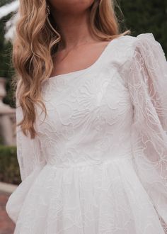 a woman wearing a white dress with long sleeves and an embellishment on her face