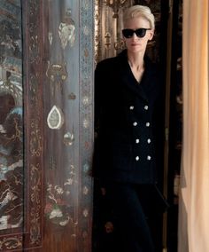 a woman standing in front of a wooden door wearing sunglasses and a black suit jacket