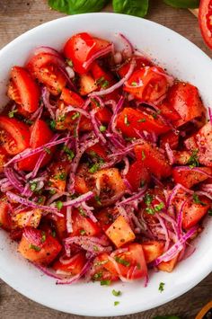 a white bowl filled with red onions and tomato salad on top of a wooden table