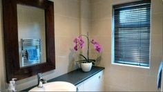 a white sink sitting under a bathroom mirror next to a window with blinds on it