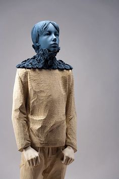 a sculpture of a man with blue hair and a scarf around his neck, standing in front of a gray background