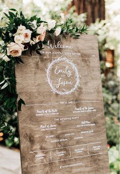 a sign that is on top of a wooden stand with flowers and greenery around it