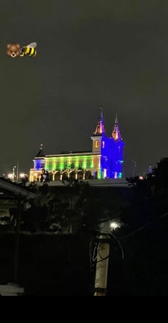 a kite flying in the air over a building with lights on it's side