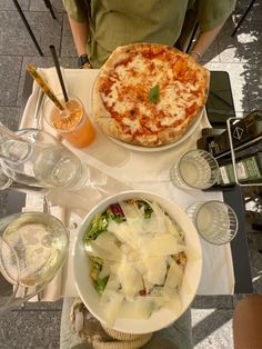 a table topped with pizza and salad next to glasses of wine on top of it