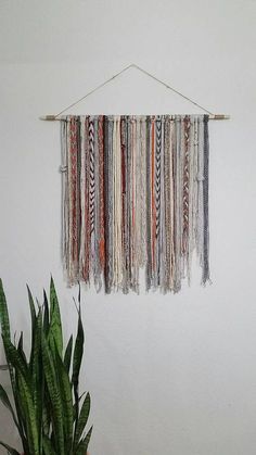 a wall hanging made out of different colored yarns next to a potted plant