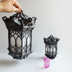 a hand holding a lit candle next to an ornate lantern