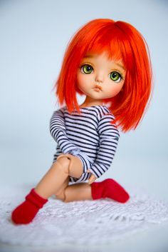 a doll with red hair and green eyes sitting on a white doily wearing socks