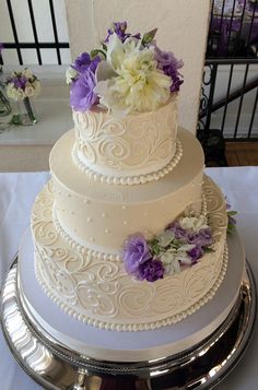 a white wedding cake with purple and white flowers on the top tier is displayed in an instagram