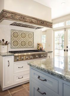 a kitchen with white cabinets and marble counter tops, an oven hood over the stove