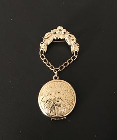 "Lovely vintage signed Monet hanging/dangling gold-tone brooch with impressed intricate floral design on the front and back of the locket, which hangs from a chain connected to a flower-and-leaf arch. (Any darker areas are reflections of us taking the photo! The pin has a polished finish.) The pin is in excellent condition and measures approx. 1.25\" across (arched pin at the top; the locket is 1\" across) and is 2.75\" long with the locket closed. See photo 3 to see the open locket; the hinge is at the base and the locket opens downward. This piece is as beautiful to wear as it would be in a collection.  We do our best to describe each selection and welcome any questions you may have. Pictures are also part of the description, so please look them over and read the entire description. Chec Vintage Medallion Brooch Jewelry, Gold Medallion Brooch For Formal Occasions, Medallion Shaped Brooch For Wedding, Medallion Brooch Jewelry For Wedding, Wedding Medallion Brooch Jewelry, Gold Medallion Brooch For Gift, Gold Locket Brooches For Gifts, Gold Pendant Locket Brooches, Heirloom Medallion Brooch