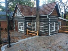 an old log cabin is sitting in the woods next to a lamp post and tree