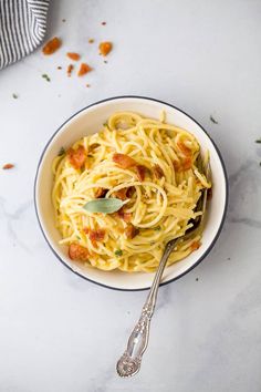 a white bowl filled with pasta on top of a marble counter next to a spoon