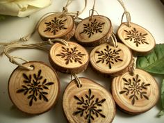 six wood slices with black snowflakes on them and some green leaves next to it