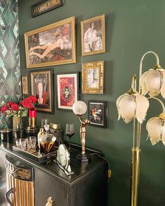 a room with green walls and pictures on the wall, including an antique cabinet filled with wine glasses