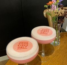 two wine glasses sitting on top of a table next to a vase filled with flowers