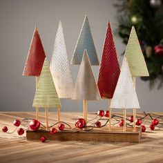 small christmas trees sitting on top of a wooden table next to a tree with red berries