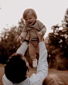 a man holding up a baby in the air with trees in the back ground behind him