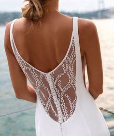 the back of a woman in a white dress looking out at water and bridge behind her