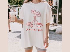 Je ne sais quoi shirt. Croissant shirt. We love how this vintage-inspired français shirt turned out, with the hand-drawn croissant, florals, and espresso. European summer vibes all the way. The graphic is distressed to give that vintage vibe. * Q U I C K * F A C T S * - 100% preshrunk cotton. - Wash and dry normally (on cool for best results ) - Comfort Colors Shirt - Direct to Garment printing for durability (no cracking). * F I T * S I Z I N G * - Unisex relaxed fit. - Crew neckline. - Size up Short Sleeve Screen Print Tops For Brunch, Short Sleeve Tops With Funny Print For Brunch, Vintage Cotton Tops For Brunch, Crew Neck Cotton Shirt For Brunch, Cotton Crew Neck Shirt For Brunch, Cotton Graphic Print Shirt For Brunch, Vintage White Top For Brunch, White Vintage Top For Brunch, Tomato Girl Summer