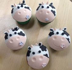 four cupcakes decorated like cows sitting on top of a wooden table with frosting