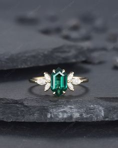 an emerald and diamond ring sitting on top of a black stone slab with white diamonds