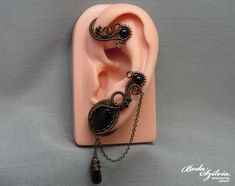 Wire wrapped gothic ear wrap with black onyx stones and chain, no piercing required. It's made of bronze artistic wire, antiqued brass chain, seed beads, an antiqued brass bezel, black onyx beads and cabochon, and a matching black glass briolette bead. One of a kind. For the left ear. You can find more ear wraps here: https://www.etsy.com/shop/bodaszilvia?section_id=10953132&ref=shopsection_leftnav_4 Plz, read my policies before buying. Thank you! If you are interested in news, work in progress Handmade Black Metal Body Jewelry, Handmade Black Ear Cuff, Black Gothic Handmade Body Jewelry, Handmade Gothic Black Body Jewelry, Handmade Black Gothic Body Jewelry, Gothic Black Body Jewelry With Adjustable Chain, Handmade Adjustable Black Ear Cuff, Handmade Black Metal Cartilage Earrings, Handmade Black Ear Cuff As Gift