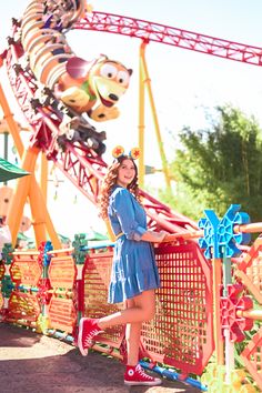 a woman standing in front of a roller coaster at an amusement park with characters on it