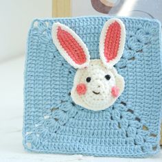 a crocheted blue square with a white bunny face on it and pink ears