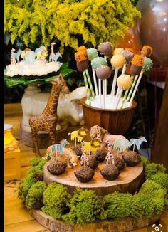 a table topped with cake pops covered in animals and jungle themed food items on top of a tree stump