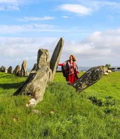 a woman standing next to large rocks in a field with grass and blue sky behind her