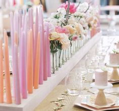 there are many candles on the table with flowers in vases next to each other