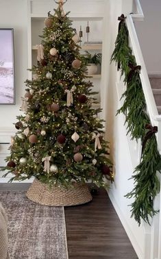 a decorated christmas tree sitting in the corner of a living room next to a stair case