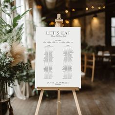 an easel with a seating chart on it in front of a table at a wedding