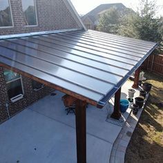 a large metal roof on top of a house next to a brick wall and yard