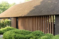 a thatched roof building with wooden slats on the side and bushes in front