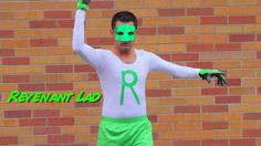 a man with green paint on his face and hands in front of a brick wall