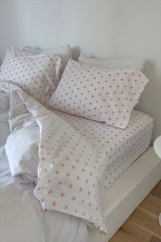 a bed with white sheets and pink hearts on it's pillowcase, along with two night stands