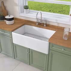 a white kitchen sink sitting under a window next to green cupboards and counter tops